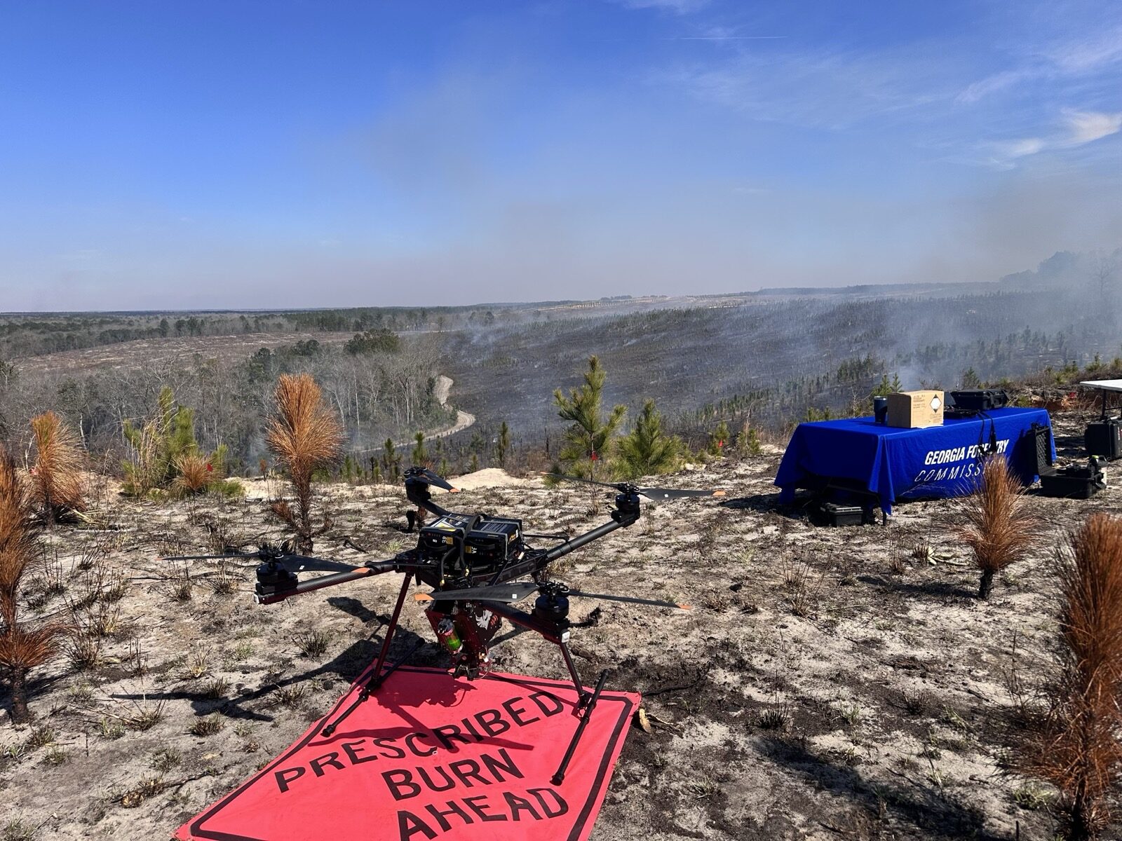 Close-up of the prescribed burn drone on a red landing pad with a "Prescribed Burn Ahead" sign